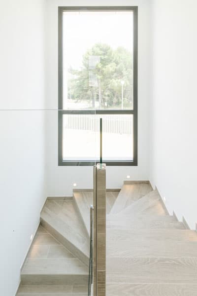 Escalera con barandillas de cristal y un gran ventanal en vivienda unifamiliar