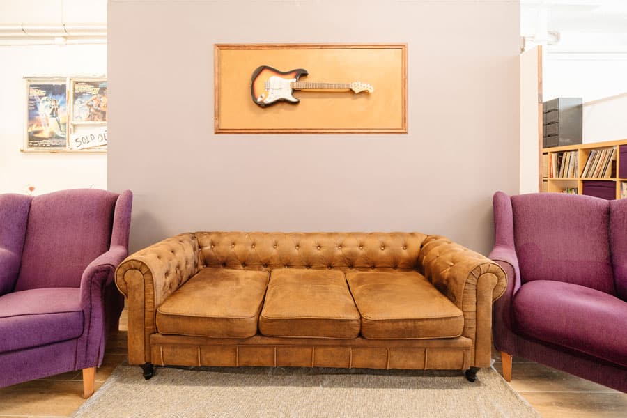 Sofá chester de color marrón con dos butacas lilas y una guitarra eléctrica enmarcada en un cambio de uso en planta baja