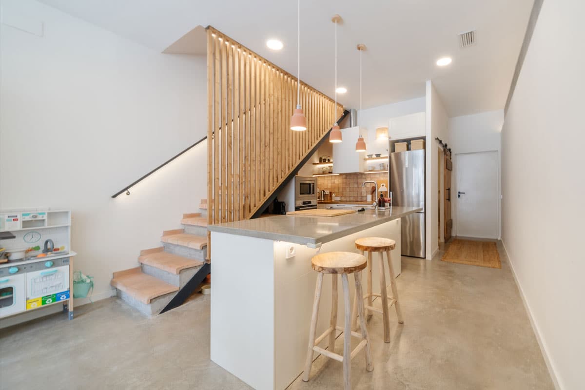 Vivienda reformada en Sabadell tras el cambio de uso, con cocina moderna de isla, escalera de madera y un diseño interior luminoso y acogedor