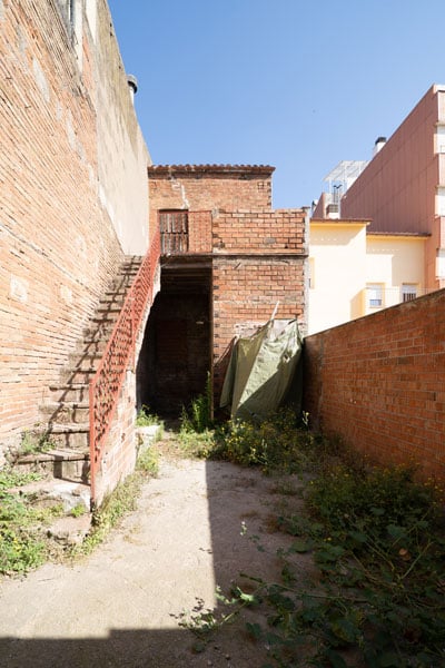 Estado original del patio en Sabadell antes de la reforma y cambio de uso, con muros de ladrillo visto, escalera metálica y vegetación sin mantenimiento