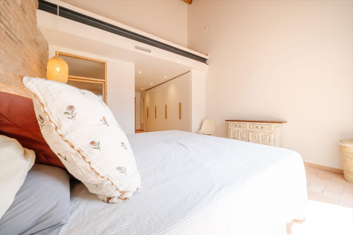 Dormitorio reformado en Sabadell tras el cambio de uso, con cama doble, armarios empotrados y diseño interior luminoso con detalles en madera