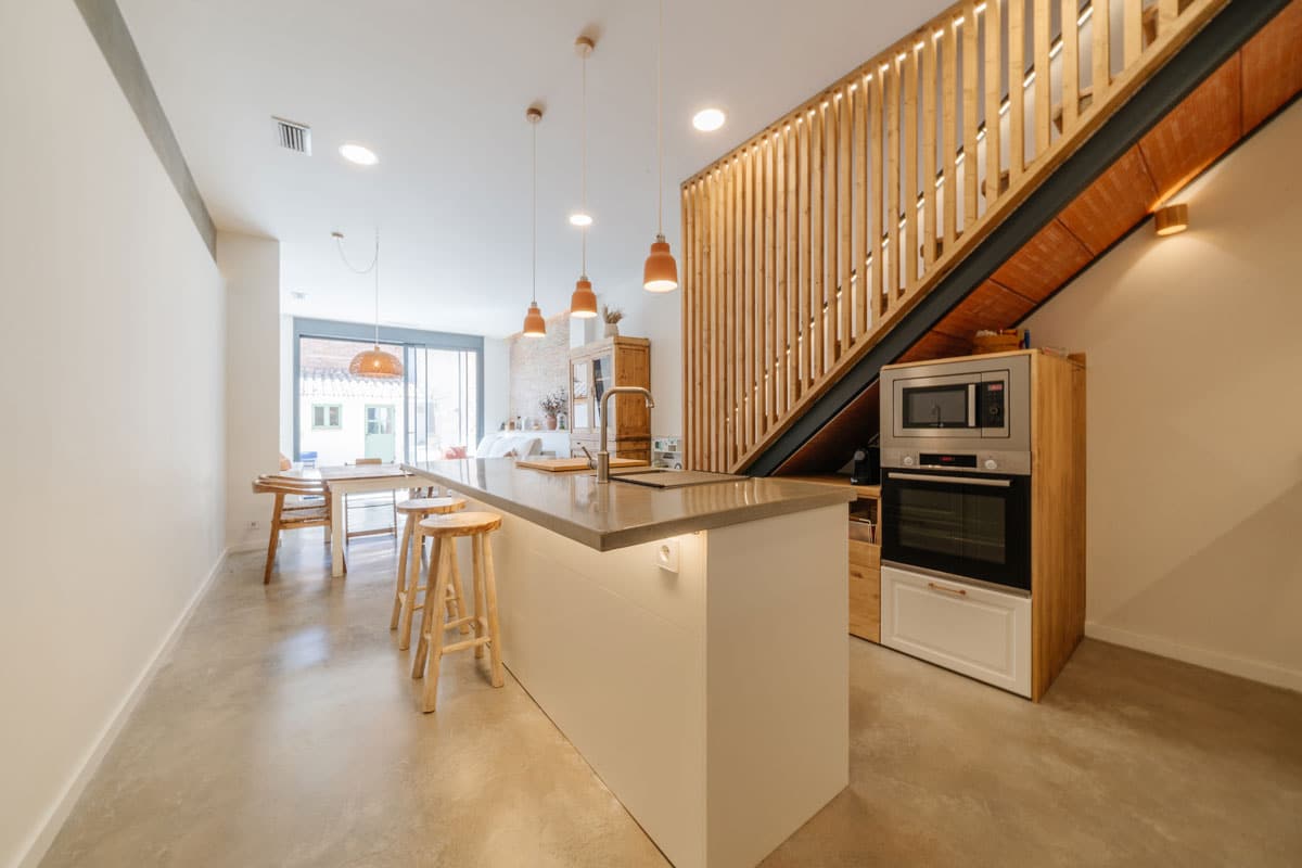Cocina abierta con isla central y comedor integrado en reforma y cambio de uso a vivienda en Sabadell. Acabados modernos en madera y microcemento