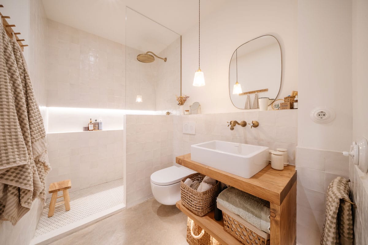 Baño reformado en Sabadell tras el cambio de uso, con ducha integrada, lavabo sobre encimera de madera y diseño cálido con materiales naturales