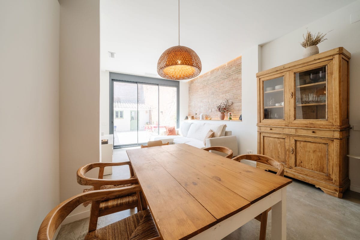 Comedor en vivienda saludable tras el cambio de uso en Sabadell, con mesa de madera, sillas de fibras naturales y salida directa al patio