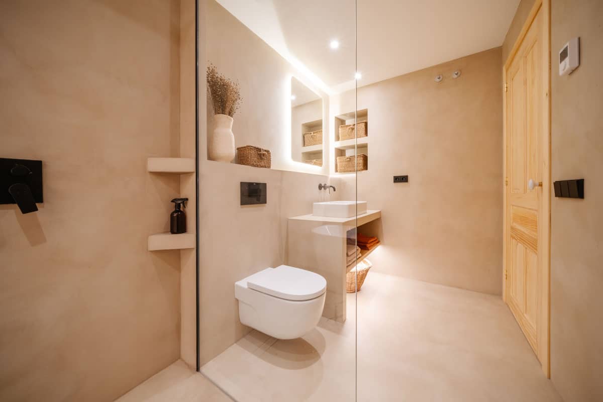 Baño reformado en vivienda saludable de Sabadell, con ducha de microcemento, sanitario suspendido y estanterías empotradas con cestos de fibras naturales