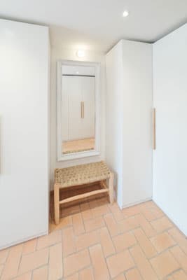 Vestidor en vivienda reformada en Sabadell tras el cambio de uso, con armarios blancos empotrados, banco de fibras naturales y espejo de pie
