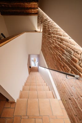 Escalera interior en vivienda reformada en Sabadell, con peldaños de barro cocido, pared de ladrillo visto y luz indirecta integrada