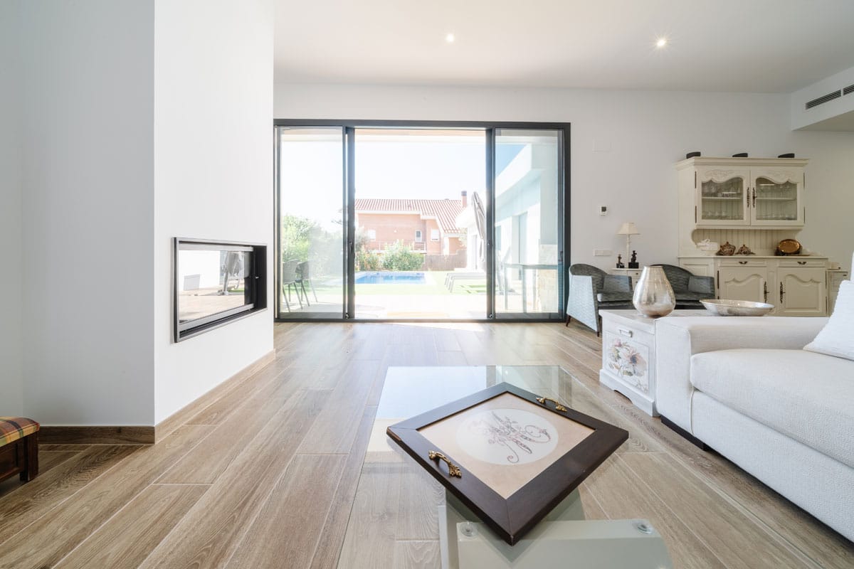 Salón con chimenea en vivienda saludable y eficiente en l’Ametlla del Vallès, con conexión interior-exterior hacia la piscina y el jardín.
