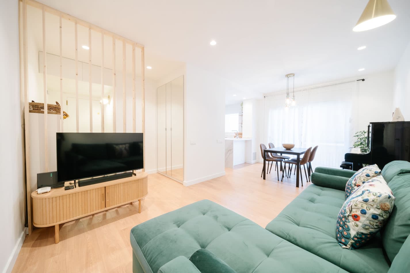 Salón comedor reformado con sofá verde, comedor junto a la ventana y separador de madera