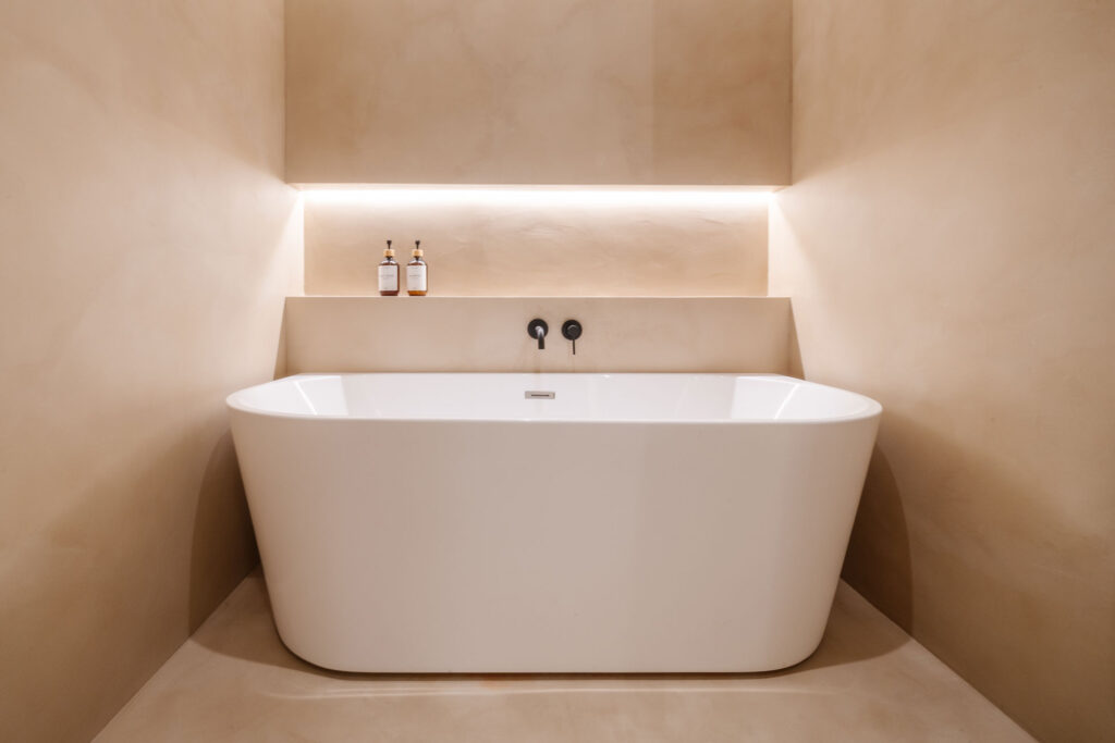 Bañera exenta bajo un nicho iluminado en baño de microcemento