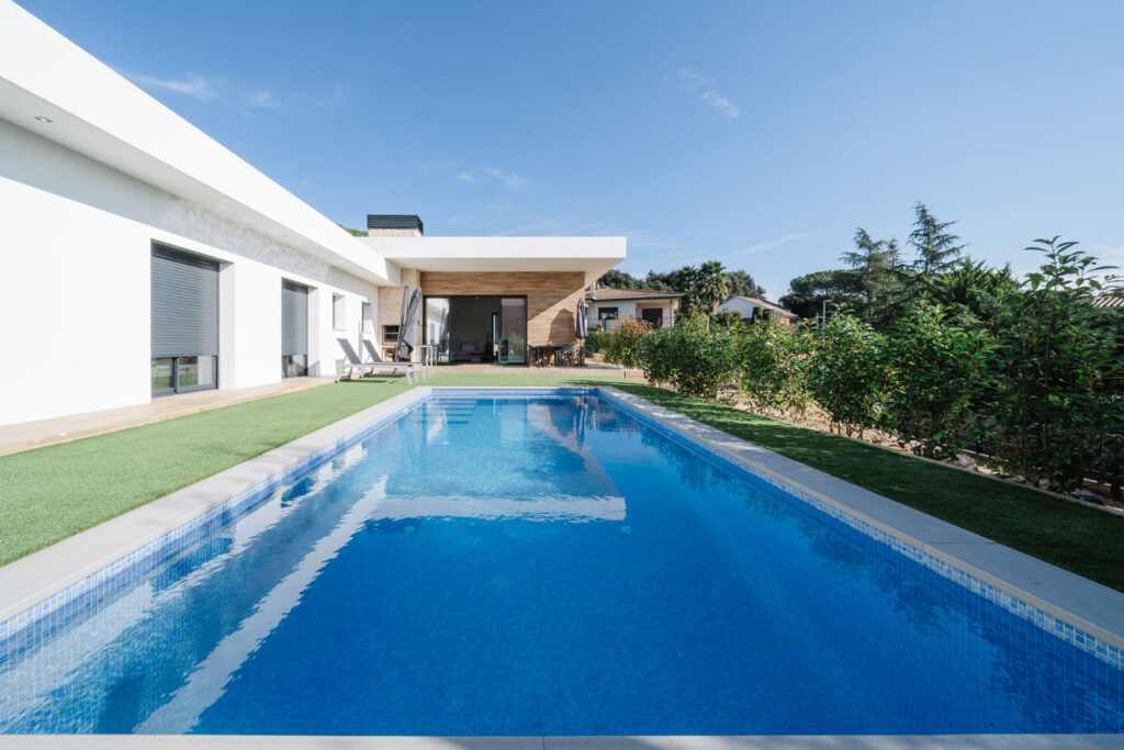 Piscina en primer plano frente a porche de casa unifamiliar moderna